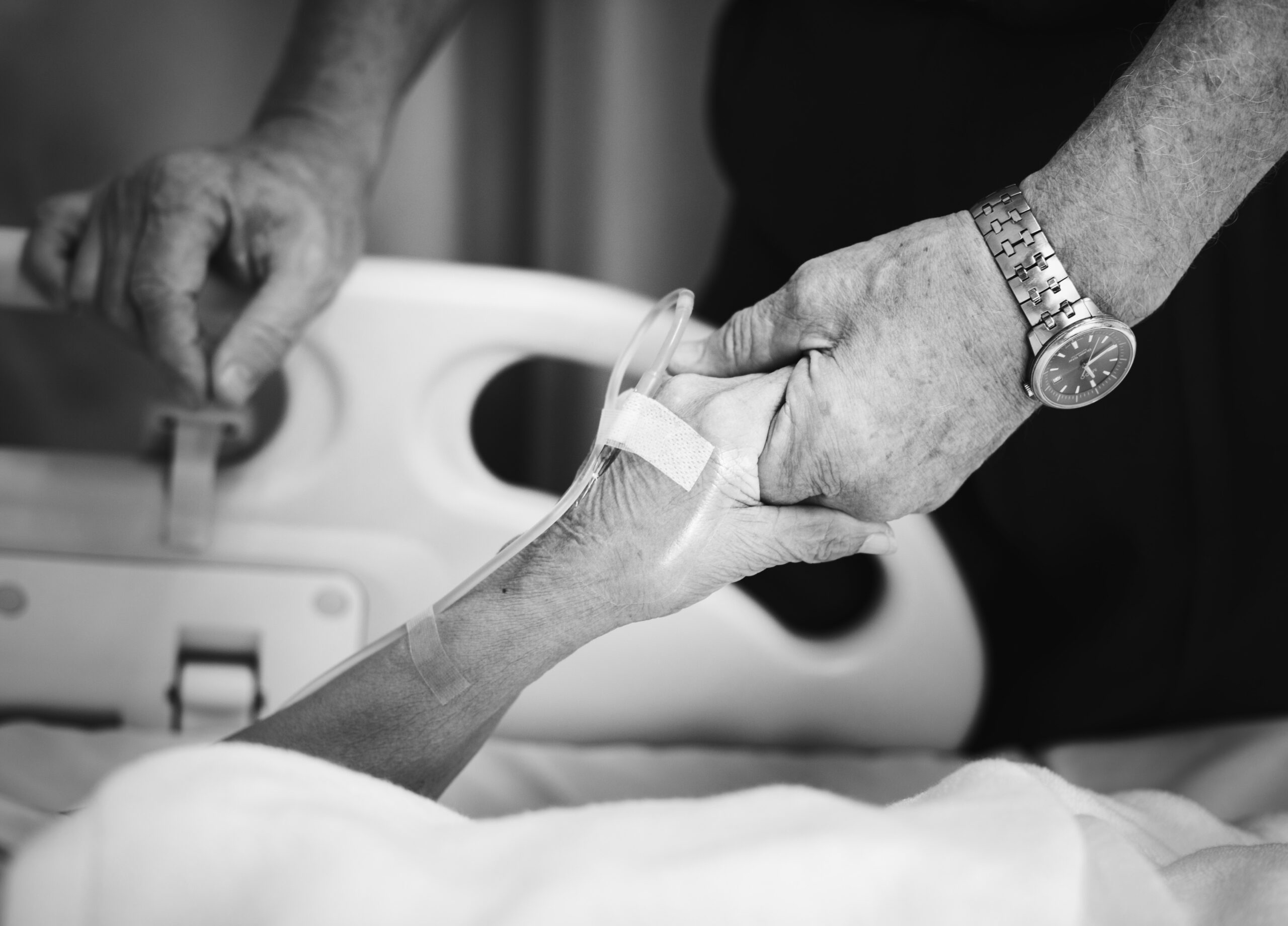 older person in a hospital bed holds someone's hand