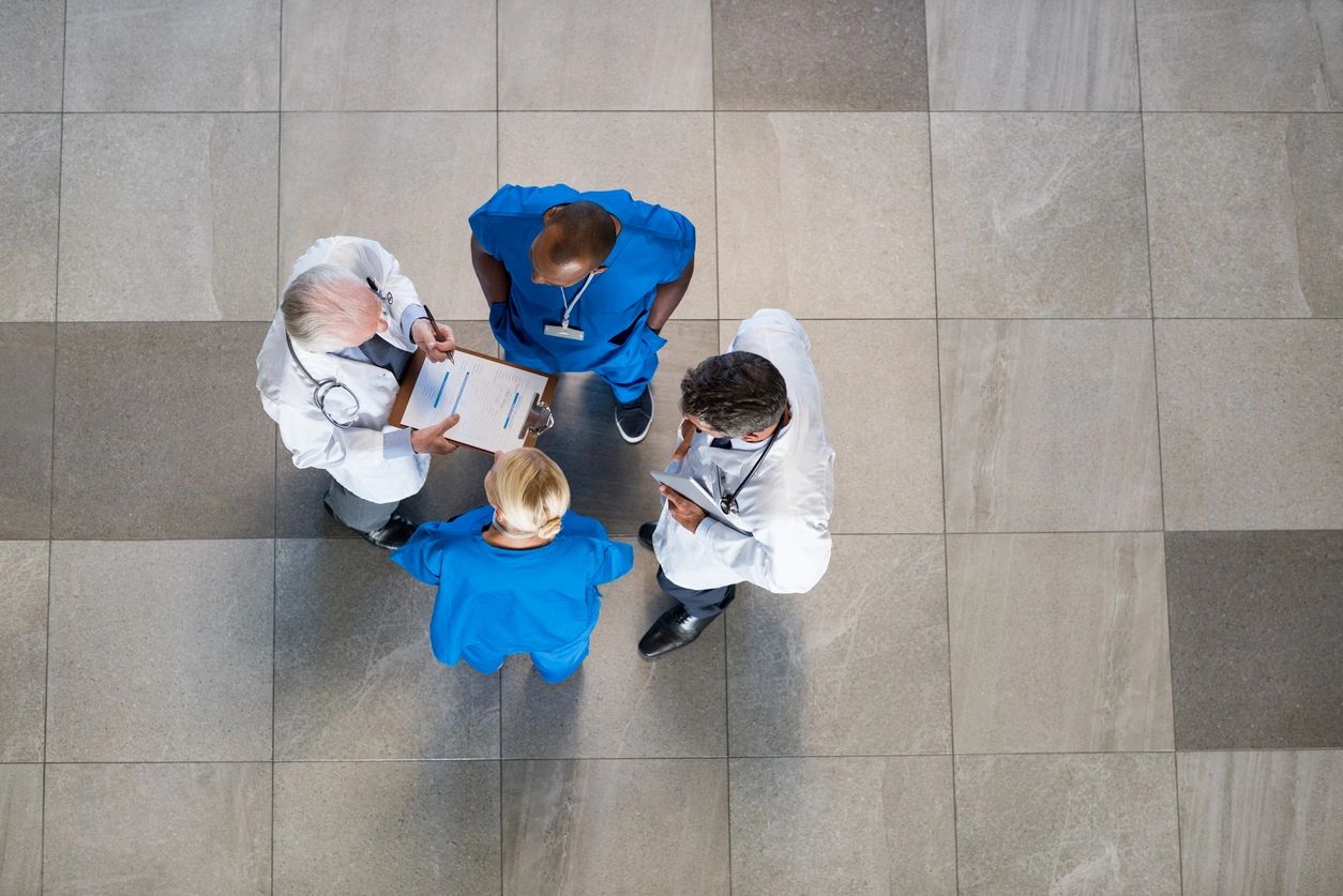 Four doctors talking as seen from above. Two with white coats and 2 in scrubs.
