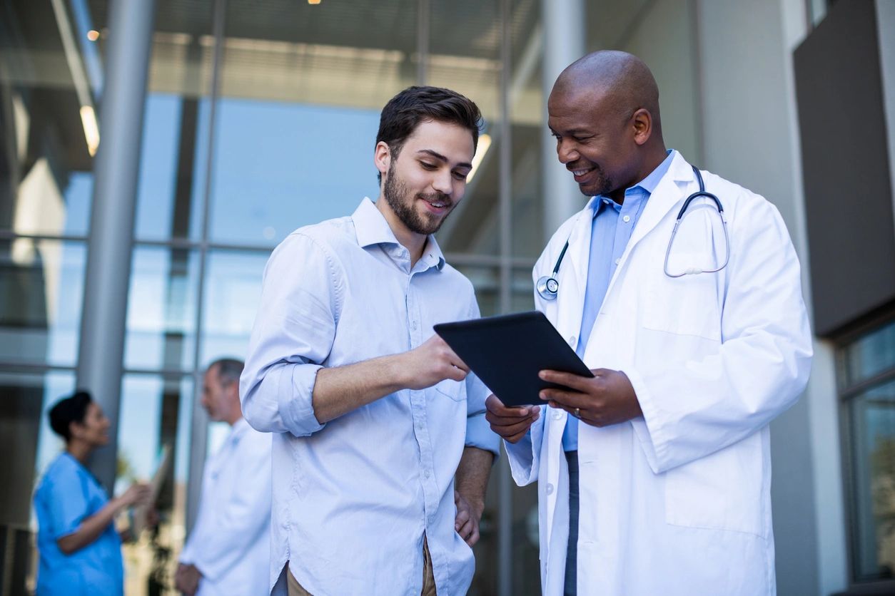 Doctor with a clipboard speaking to a man outside of a hospital