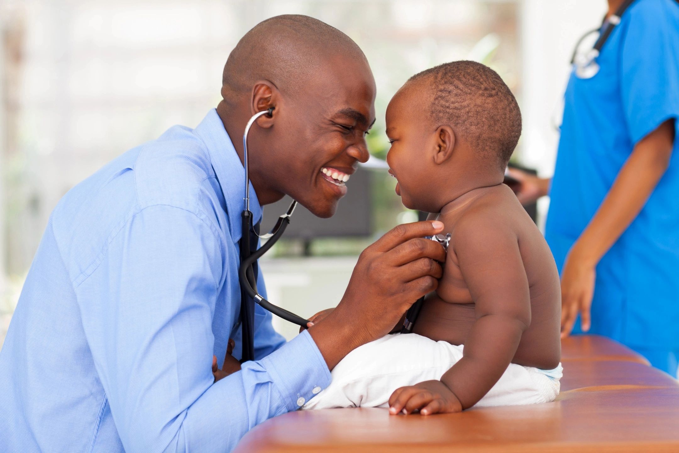 Individual with stethoscope and young child on exam table