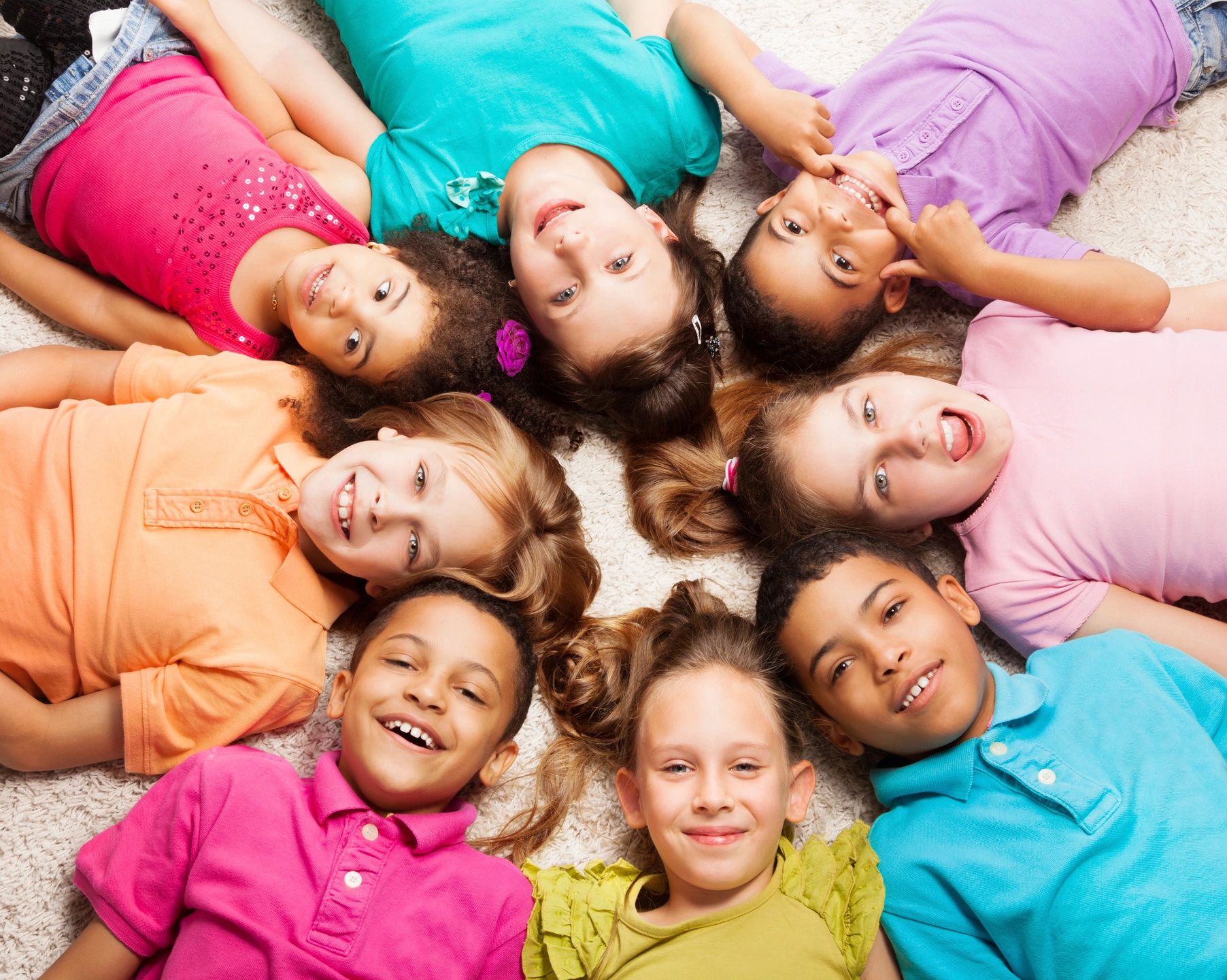 Eight kids laying in a circle looking up at camera